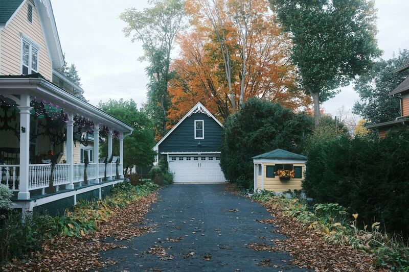 Leaf-covered driveway leading to a detached garage with white door and autumn trees