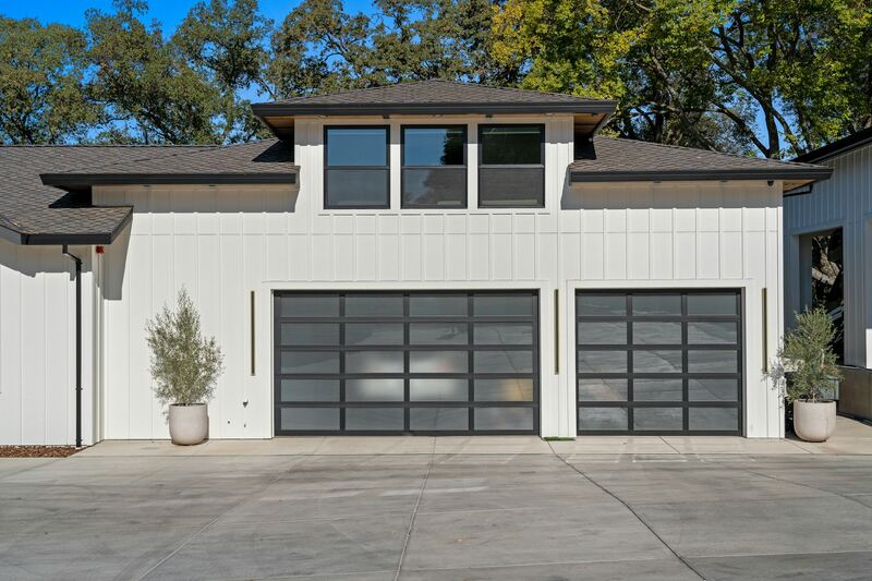 Two modern frosted glass and black aluminum garage doors on a white board-and-batten home