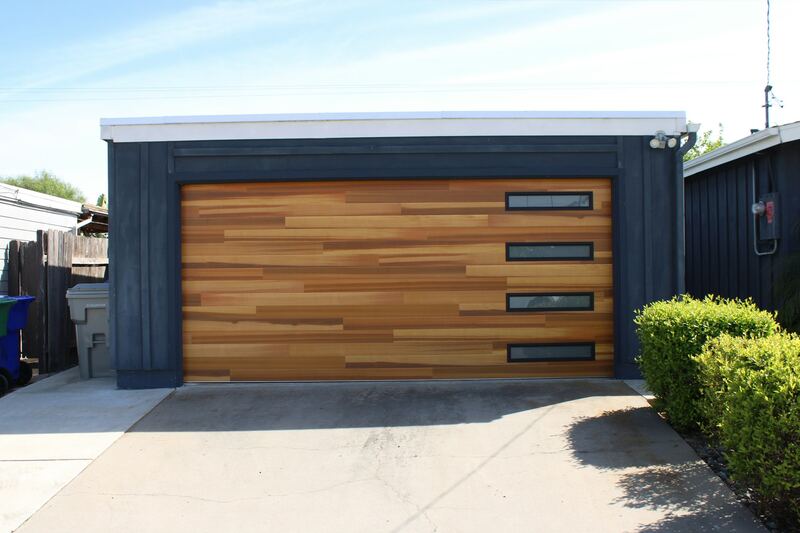 Modern wood-grain garage door with vertical window strip on a dark-painted garage
