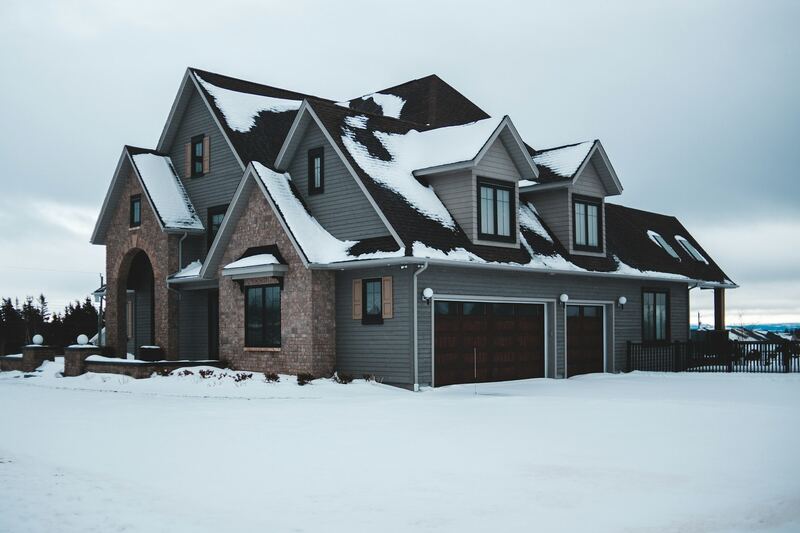 Stone and gray-sided home in winter snow with two dark wood-look garage doors